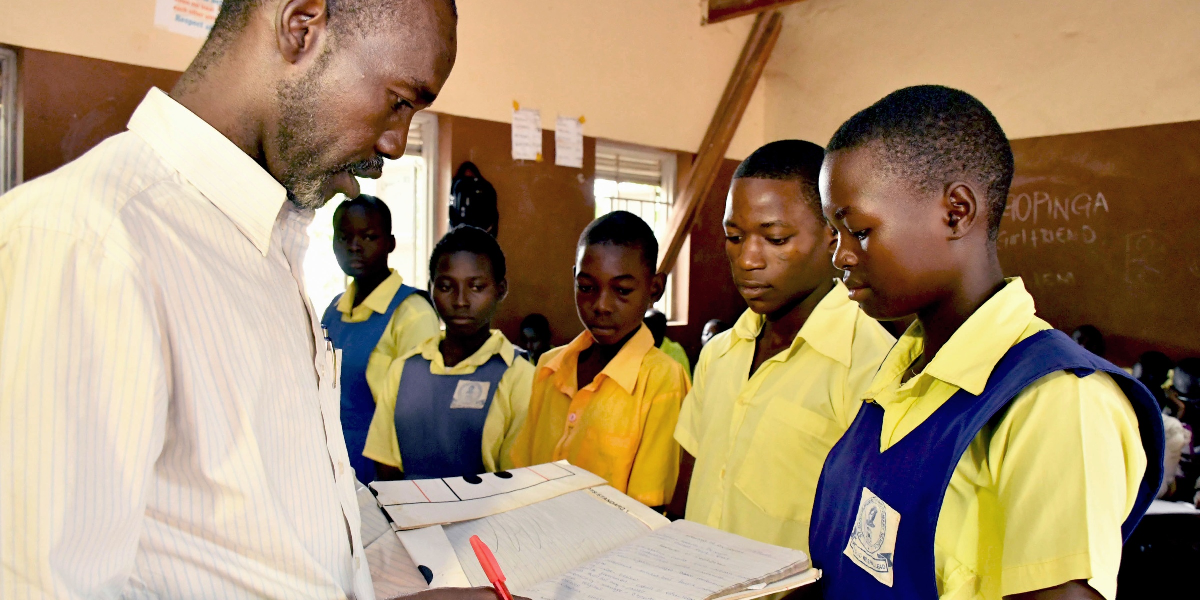 Teacher Adam Gabriel checks the work of his students Moses Justin, Daniel Adam and Salawa Emmanuel during a history lesson at St. Bakhita Primary School. Credit: GPE/Jok Solomon